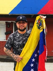Photo of male holding the Venezuela flag in front of business