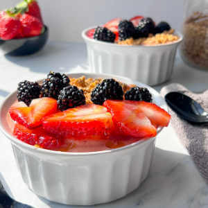 Two smoothie bowls with fruit and spoons next to bright window