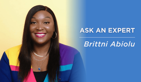 Brittni Abiolu Ask and Expert member and entrepreneur wearing a multicolored sweater in front of a yellow backdrop