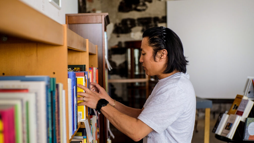 A man wearing a light grey shirt puts books on a bookshelf