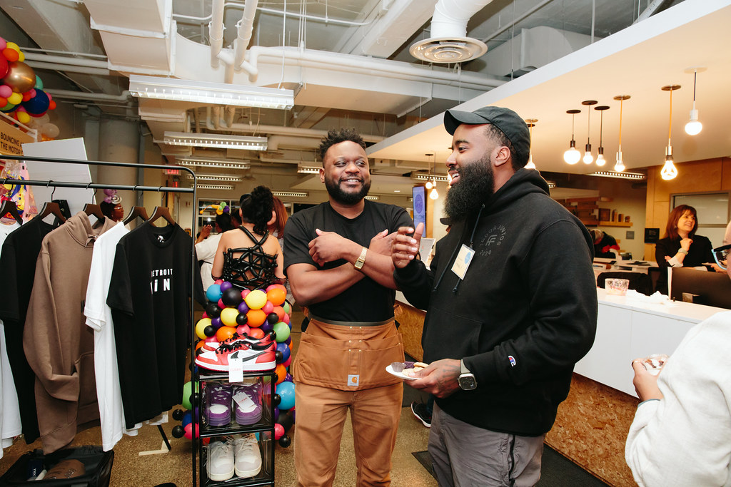 Two men of color talk by a rack of clothing