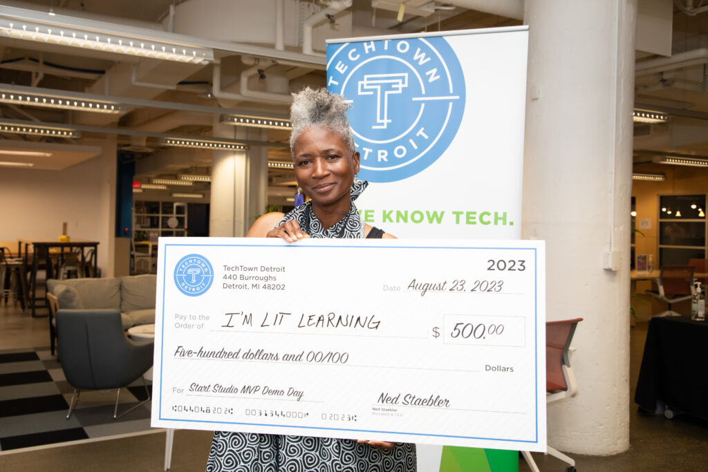 A woman of color holds a large check for $500, for her business, I'M LIT Learning