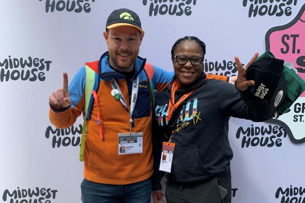 Two people pose and smile for a photograph in front of a white-and-black step-and-repeat for the Midwest House, during an event for the 2024 South by Southwest conference