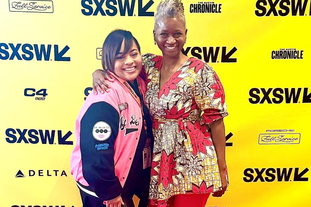 Two people pose and smile for a photograph, standing in front of a yellow-and-black step-and-repeat at a 2024 South by Southwest event