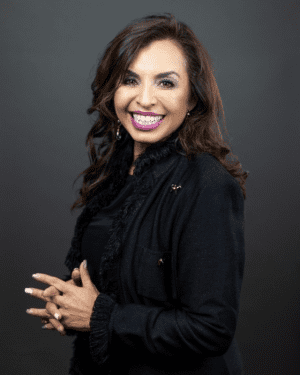 A woman smiles for a headshot with her hands clasped together