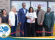 A photo of several people standing outside the new location for Genesis Therapeutic Massage and Bodywork, they stand behind a large ribbon and the person in the middle has cut the ribbon with a large pair of scissors. Overlapping this photo is TechTown Detroit's 20th anniversary logo