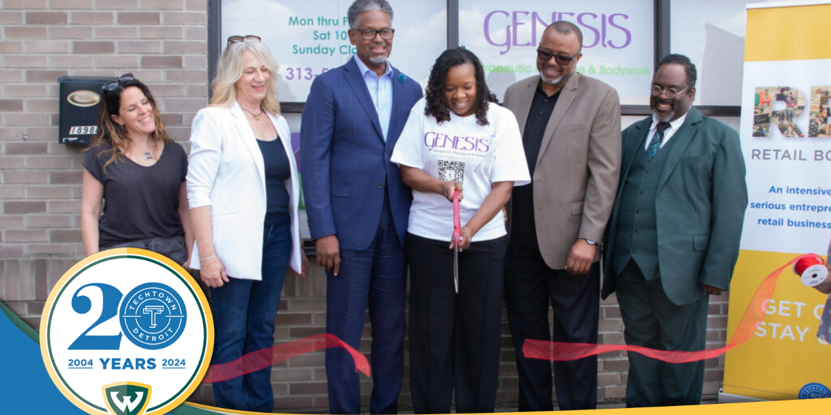 A photo of several people standing outside the new location for Genesis Therapeutic Massage and Bodywork, they stand behind a large ribbon and the person in the middle has cut the ribbon with a large pair of scissors. Overlapping this photo is TechTown Detroit's 20th anniversary logo