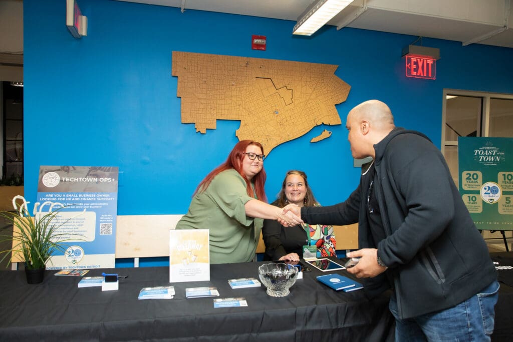 A photo of a TechTown team member shaking hands with someone at an Ops+ informational table