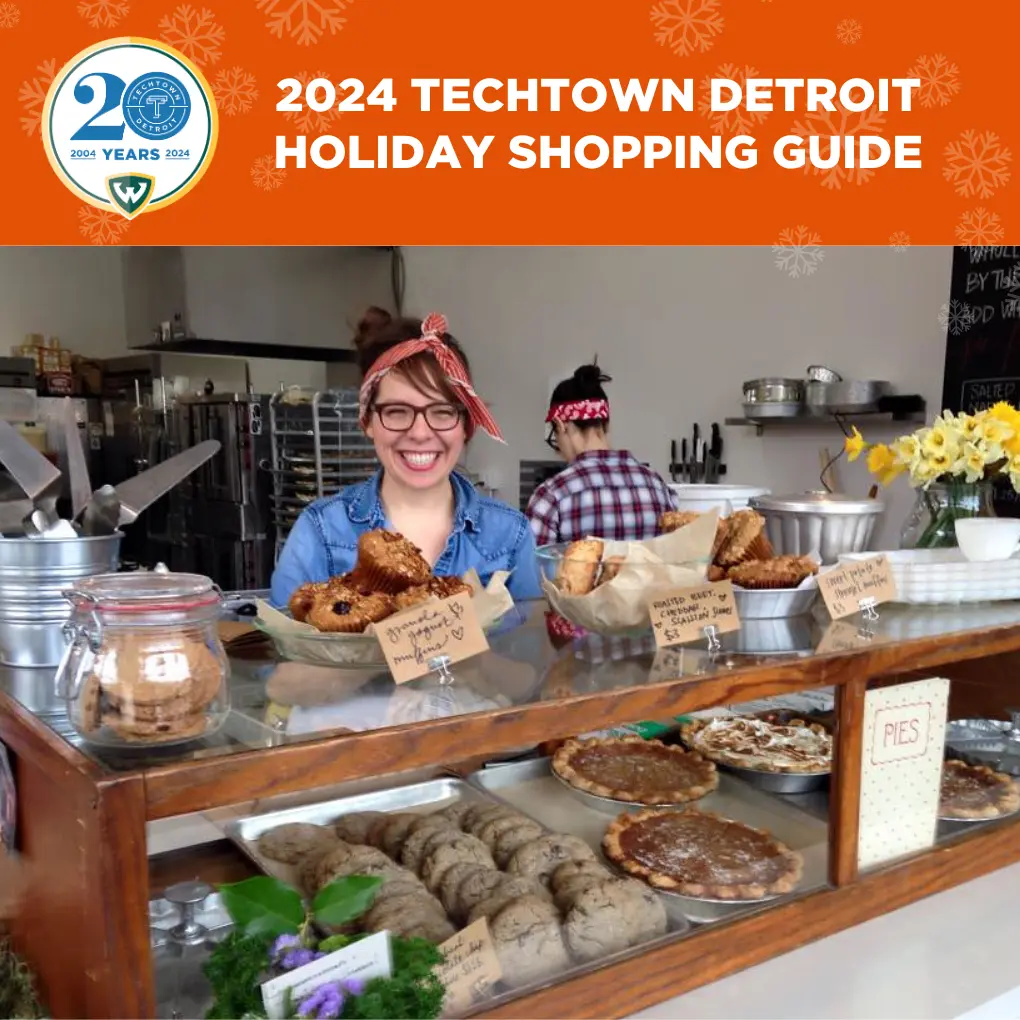 Un gráfico que dice &quot;2024 TechTown Detroit Holiday Shopping Guide&quot;. Debajo de esta copia hay una foto de Lisa Ludwinski, chef y propietaria de Sister sonriendo y de pie detrás de un expositor de pasteles y otros productos horneados en su panadería