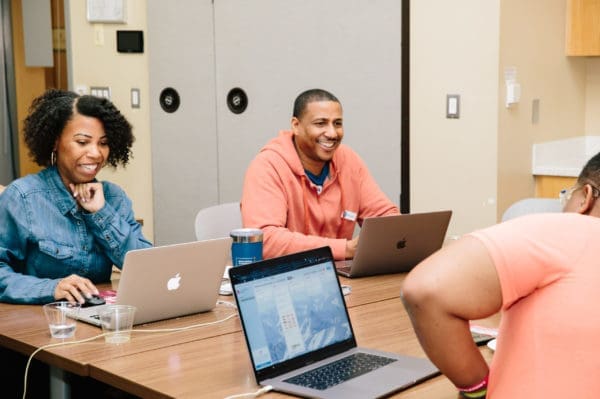 Participants sitting at a table working on laptops and smiling.