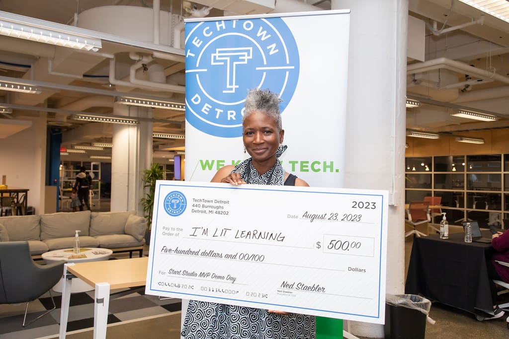 Una mujer sostiene un gran cheque de TechTown Detroit por valor de 500 dólares para su nueva empresa, I&#039;M LIT Learning.