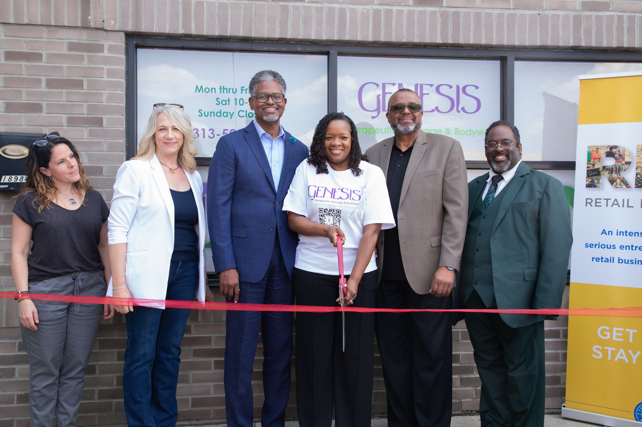 A business on their opening day, with the owners holding large scisors to cut a red ribbon.