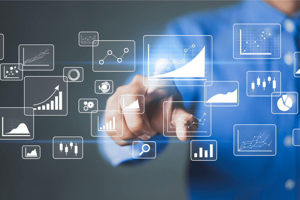 In the background of an image features a person wearing a blue dress shirt, pointing. In the foreground are floating icons of charts and graphs. The pointed finger taps on an icon of a graph and there is a light illuminating from the person's finger.