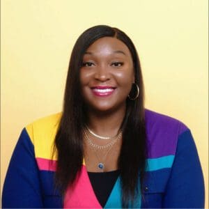 Brittni Abiolu Ask and Expert member and entrepreneur wearing a multicolored sweater in front of a yellow backdrop 