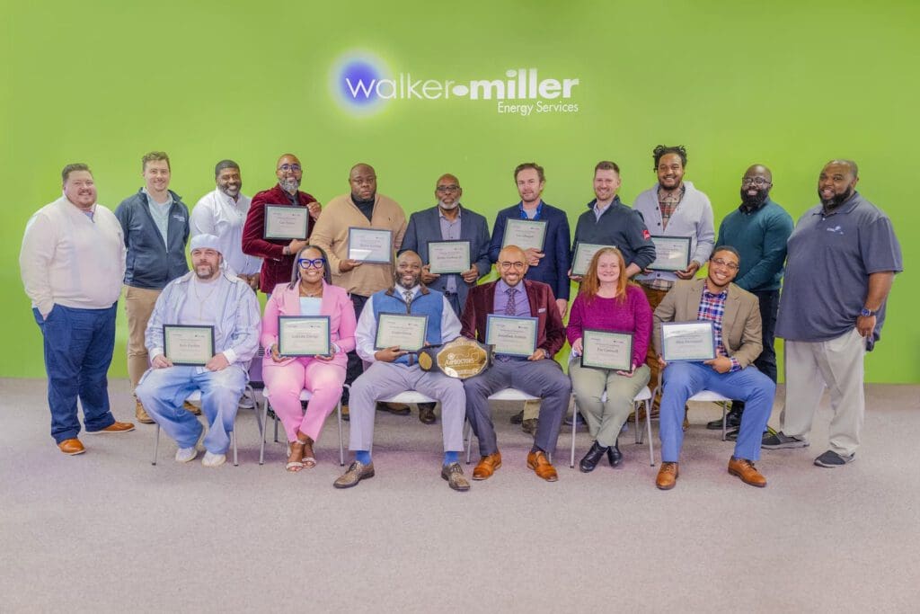 A group of people sitting and smiling for a photograph. The majority of them hold plaques. On the wall behind them is a sign for Walker-Miller Energy Services