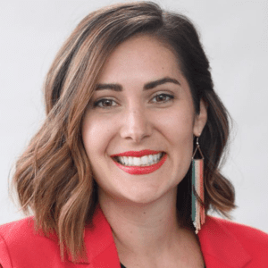 A woman smiling for a headshot, wearing a red blazer and a green/white/red-beaded earring