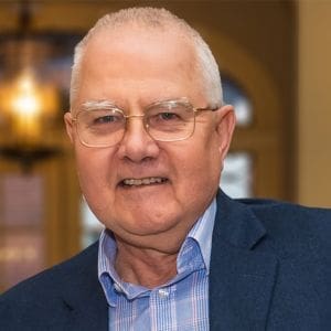 A man smiling for a headshot, wearing a navy blue suit jacket and a light blue patterned dress shirt