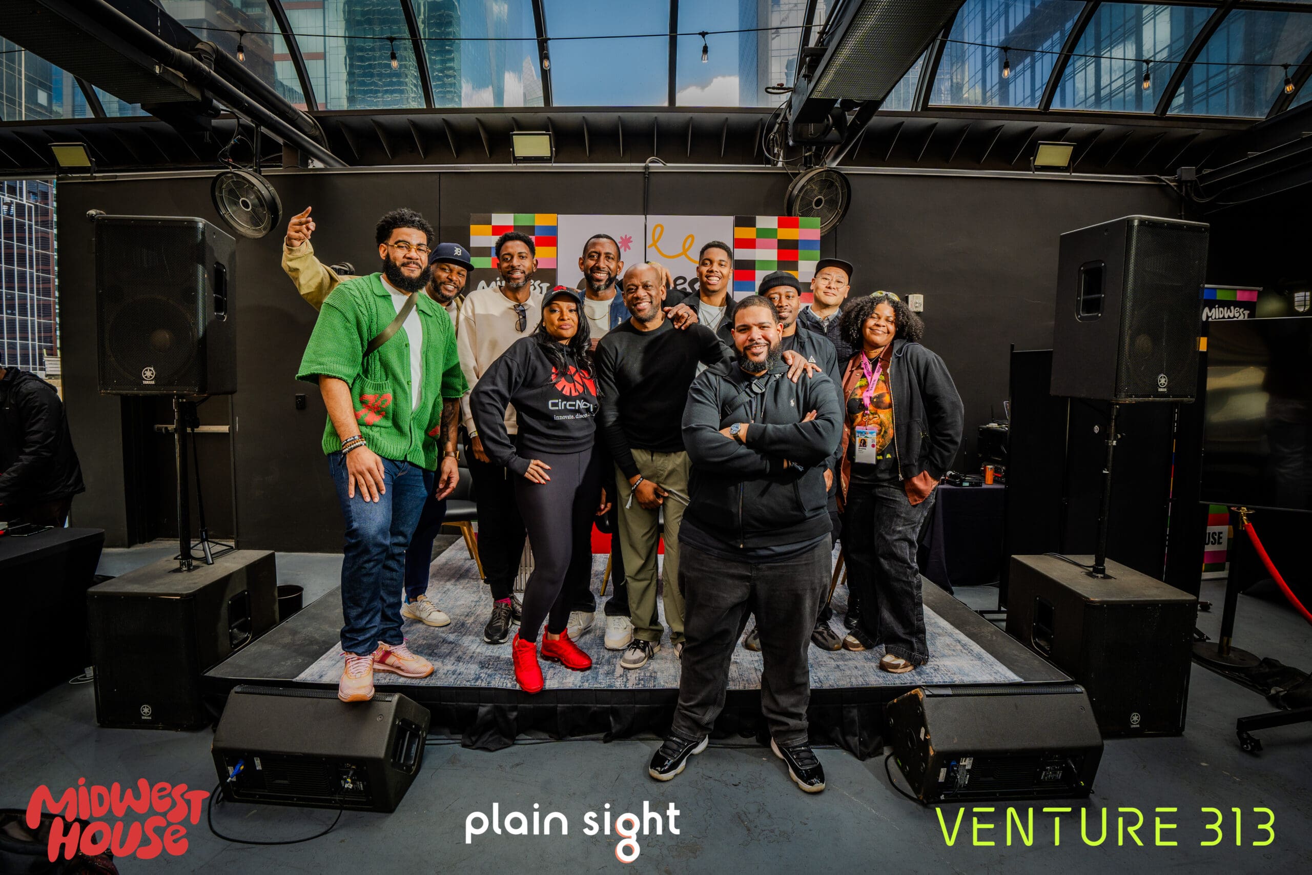 A group of people standing on a stage, surrounded by sound equipment. They all smile and pose. Overlapping the photo are images of the logos for Midwest House, Plain Sight and Venture 313